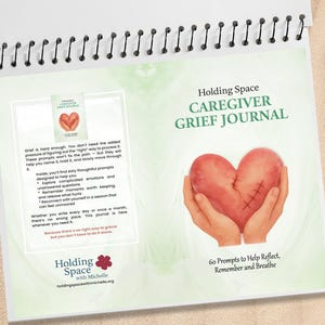 May include: A spiral-bound journal titled "Holding Space Caregiver Grief Journal." The cover features a heart held in hands, with text indicating 60 prompts to help reflect, remember, and breathe. The journal's pages include text about processing grief.