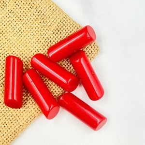 Puede incluir: Un grupo de seis cuentas cilíndricas rojas, algunas de las cuales están parcialmente ocultas por una bolsa de arpillera marrón.