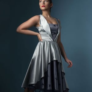 May include: A silver satin dress with a layered skirt and a black lace trim. The dress has a sweetheart neckline and a fitted bodice.