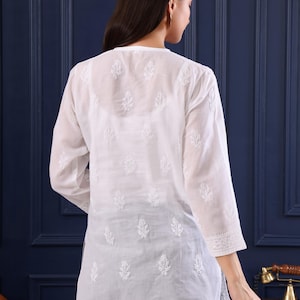 May include: White, long-sleeved tunic with intricate embroidered leaf patterns. The tunic has a V-neck and three-quarter sleeves. The brand name "Jeehva" and the tagline "Threads that breathe tradition" are visible in the upper right corner.