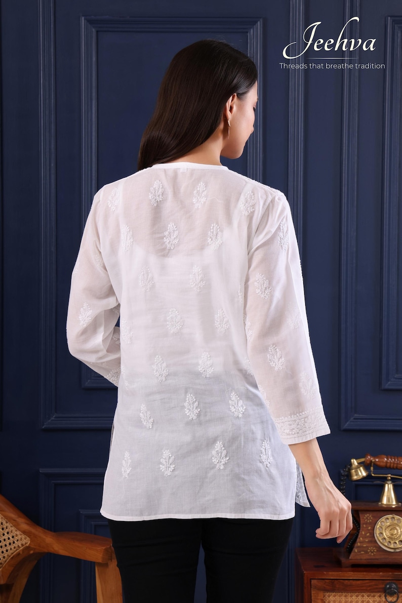 May include: White, long-sleeved tunic with intricate embroidered leaf patterns. The tunic has a V-neck and three-quarter sleeves. The brand name "Jeehva" and the tagline "Threads that breathe tradition" are visible in the upper right corner.