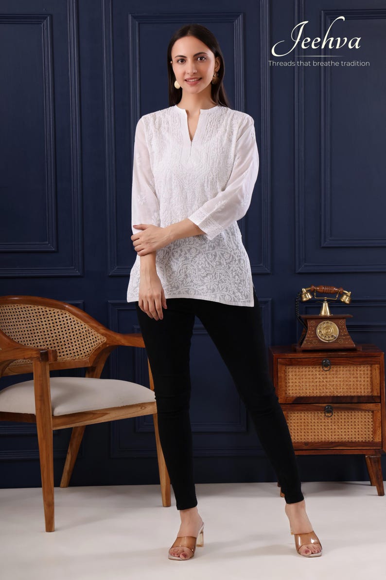 May include: A woman wearing a white embroidered tunic and black pants. The tunic has a V-neck and three-quarter sleeves. The image includes the text "Jeehva Threads that breathe tradition".