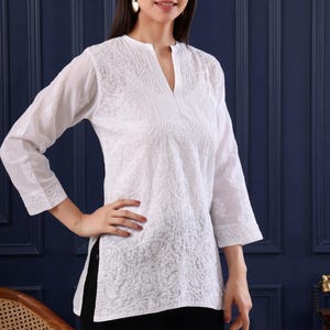 May include: White embroidered tunic with a V-neck and three-quarter sleeves. The tunic features intricate floral patterns and the text "Jeehva Threads that breathe tradition". The model is wearing black pants.