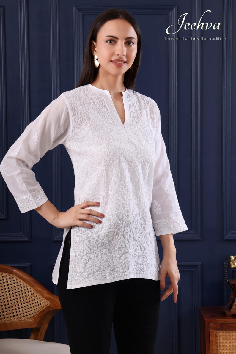 May include: White embroidered tunic with a V-neck and three-quarter sleeves. The tunic features intricate floral patterns and the text "Jeehva Threads that breathe tradition". The model is wearing black pants.