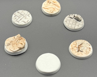 May include: Six small, round miniature bases with textured surfaces. The bases are predominantly off-white, with details in brown and grey, including cobblestone and cracked earth patterns. Each base has a diameter of approximately 2.5 cm.