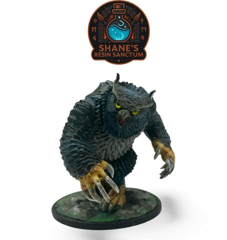 May include: A painted miniature figurine of an owlbear creature with dark blue-black feathers, yellow eyes, and tan-coloured claws, standing on a circular base. Above the figure is a logo reading SHANE'S RESIN SANCTUM with a potion bottle.