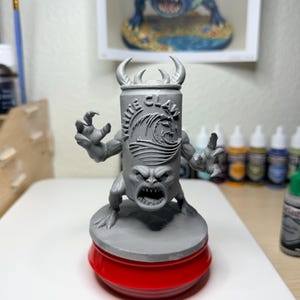 May include: A grey resin miniature figure of a monster with a White Claw can for a torso, featuring a wave logo, sharp teeth, and clawed hands. The figure stands on a circular base atop a red plastic stand, showcasing detailed sculpting.