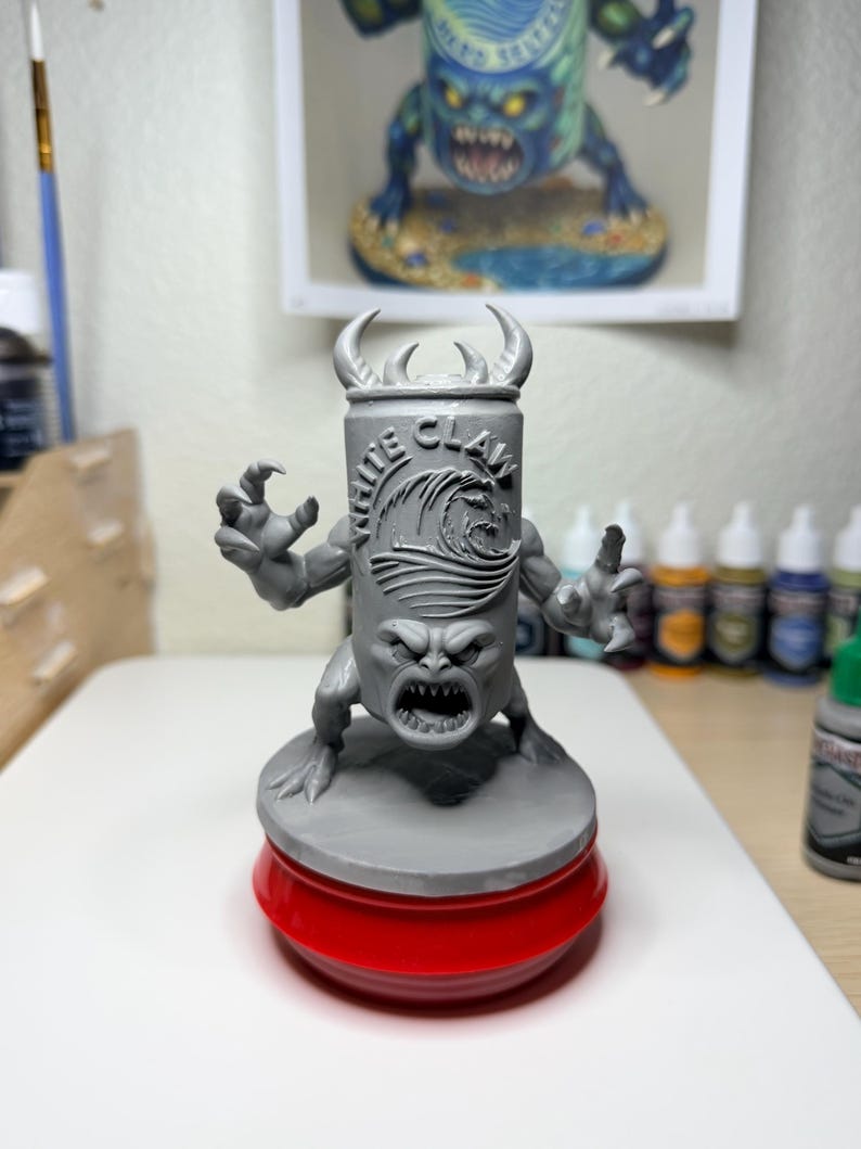 May include: A grey resin miniature figure of a monster with a White Claw can for a torso, featuring a wave logo, sharp teeth, and clawed hands. The figure stands on a circular base atop a red plastic stand, showcasing detailed sculpting.