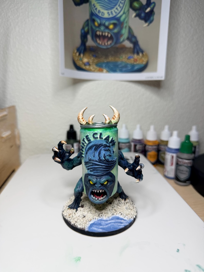 May include: A hand-painted miniature figurine of a monster with a White Claw hard seltzer can for a torso. The creature has dark blue skin, sharp claws, yellow eyes, and a wide mouth with teeth. It stands on a circular base with sand and water.