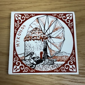 May include: Square ceramic tile featuring a detailed illustration of a Mykonos windmill with a pelican. The windmill has a thatched roof and a large, open sail. The tile is bordered with a decorative red and white design, and the word "MYKONOS" is written in red.