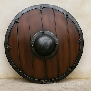 May include: A round wooden shield with a dark brown finish and a metal rim. The shield features a central, riveted metal boss and is approximately 30 inches in diameter. The shield has a rustic, antique appearance.
