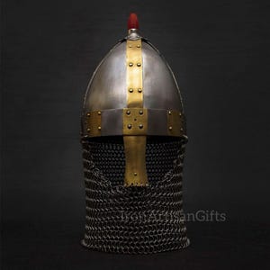 May include: A medieval-style helmet with a silver-colored dome, accented with gold-colored bands and rivets. The helmet features a red finial and a chainmail neck guard, showcasing historical craftsmanship.
