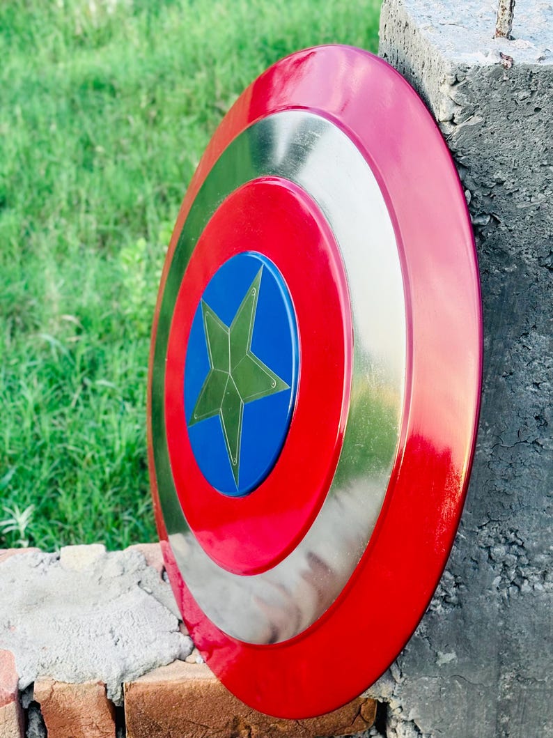 K&ouml;nnte beinhalten: Ein kreisf&ouml;rmiger Schild in Rot, Silber und Blau mit einem Sternemblem. Der Schild hat einen roten Au&szlig;enring, einen silbernen Mittelring und eine blaue Mitte mit einem goldenen Stern. Er lehnt an einer Betonstruktur.
