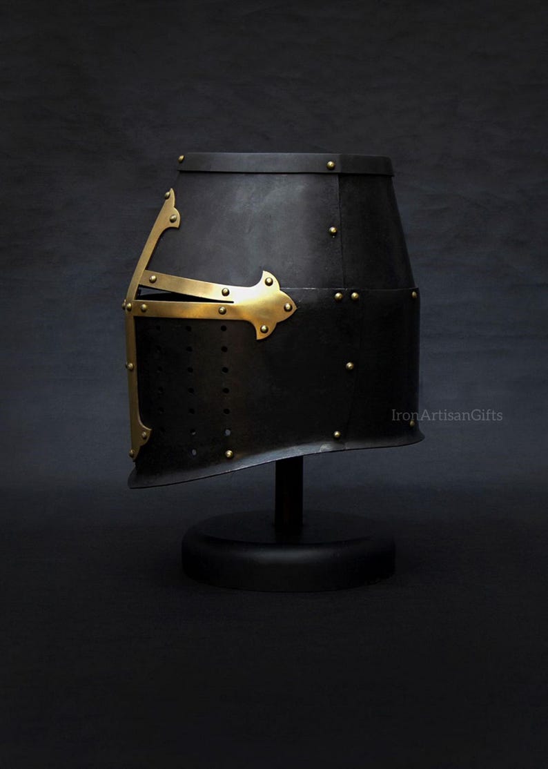 May include: Black medieval helmet with brass accents, rivets, and a cross design. The helmet is displayed on a black stand against a dark background. The product is from IronArtisanGifts.