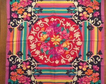 May include: A square silk scarf with a colorful striped pattern and floral designs. The center of the scarf features a large circle with a red background and a floral design.