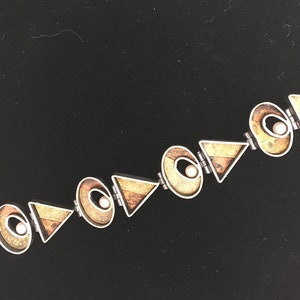 May include: A silver bracelet featuring geometric shapes and white pearls. The bracelet is crafted from metal and has a contemporary design.