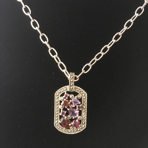 May include: A silver chain necklace with a pendant featuring a cluster of pink and red gemstones set in a silver frame with a marquetry design.
