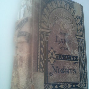 May include: A vintage book titled "Arabistan, or the Land of the Arabian Nights" with a gold and black cover and intricate design.