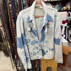 May include: A light blue denim jacket with a tie-dye pattern. The jacket has a button-up front and two pockets on the chest.
