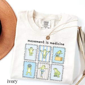 green frogs doing therapy exercises on a Comfort Colors® t-shirt with “movement is medicine” text with stamps design, printed on soft cotton shirt in various earthy tones