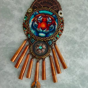 May include: A beaded necklace with a copper and turquoise pendant featuring a tiger face. The pendant has a fringe of copper tubes and a copper feather charm.