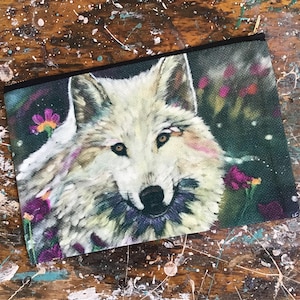May include: A white wolf with a black nose and green eyes is depicted in a colorful floral setting. The wolf is surrounded by pink, purple, and yellow flowers. The background is a dark green with a blurred effect.