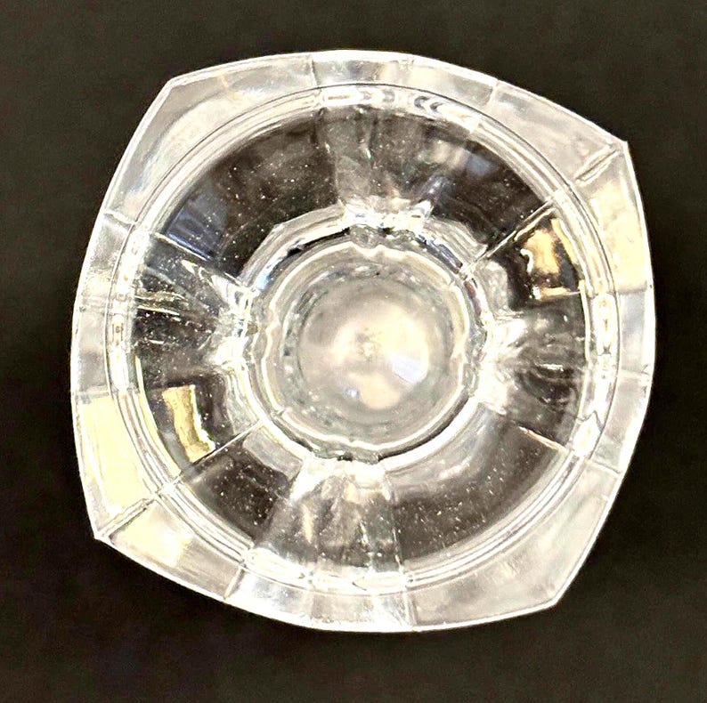 May include: Clear glass decorative bowl with a square shape and a circular interior. The bowl has a textured surface and is designed with a series of radiating lines. The bowl is transparent, allowing light to pass through.