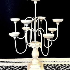 May include: A white metal candelabra with multiple candle holders. The candelabra has a decorative base and curved arms, and is painted in a distressed white finish. The design is suitable for a variety of home decor styles.