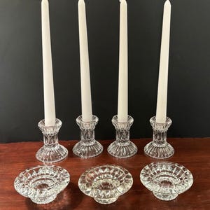 May include: A collection of clear glass candle holders with white taper candles. The set includes four upright candle holders and three matching low-profile candle holders, all with a cut-glass design. The candles are approximately 10 inches tall.