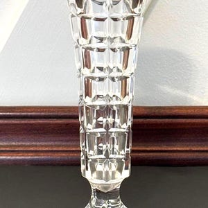 May include: A clear, faceted glass vase with a flared top and a pedestal base. The vase has a geometric, grid-like pattern and is approximately 8 inches tall.