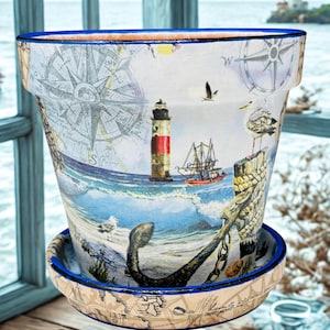 May include: A decorative ceramic flower pot with a nautical theme. The pot features a detailed illustration of a lighthouse, a ship, and a compass rose. The pot has a blue rim and a matching saucer, perfect for coastal decor.