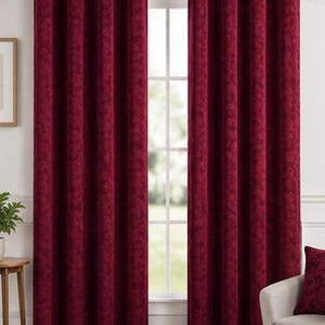 May include: A pair of deep red curtains featuring a subtle tonal leaf pattern. The curtains are hung on a silver-toned metal rod using integrated silver eyelets, creating uniform vertical folds that extend from the top to the floor.