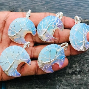 May include: Five handcrafted pendants featuring a tree of life design. Each pendant has a silver wire tree design over a blue and white opal-like stone. The pendants are crescent-shaped with a silver loop at the top.