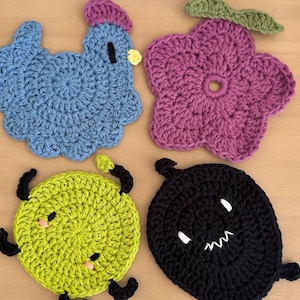 Peut inclure: Quatre dessous de verre faits à la main au crochet de différentes formes. Un poulet bleu, une fleur violette, une créature vert citron avec des antennes noires et une créature noire avec des dents blanches. Chaque dessous de verre est en fil.