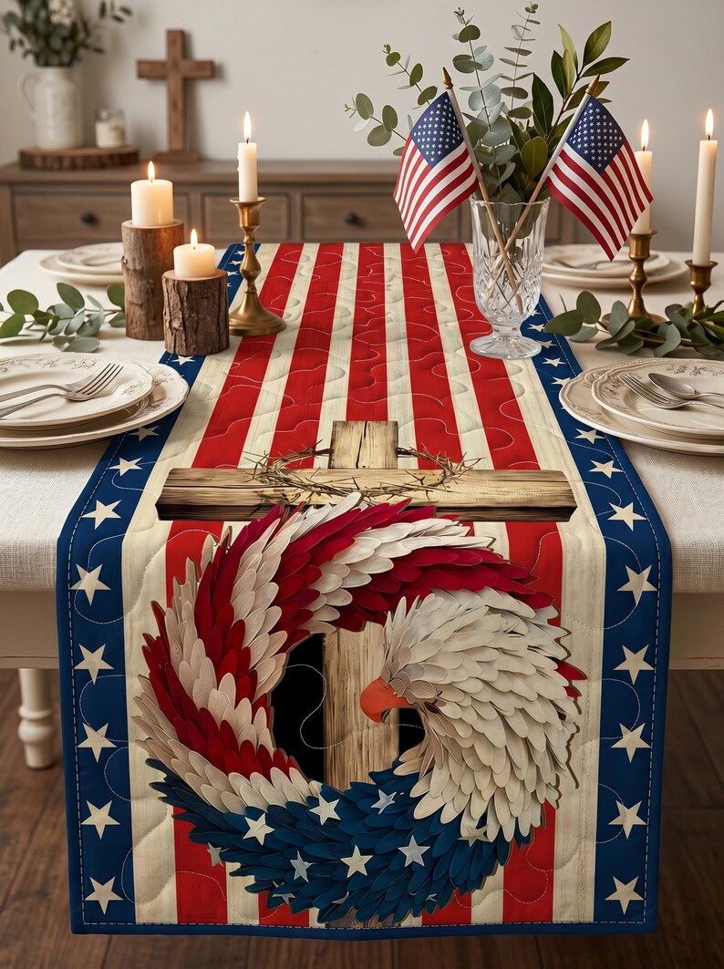 May include: A patriotic table runner featuring a design of the American flag with red and white stripes, blue borders with white stars, and a central image of a cross and eagle wreath. The table is set with candles and American flags.