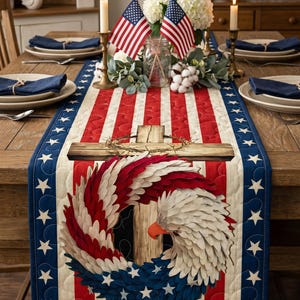 May include: A patriotic table runner with a red, white, and blue design. The center features a cross and an eagle with a wreath of feathers. The runner is bordered with blue fabric and white stars. The table is set with plates, napkins, and candles.