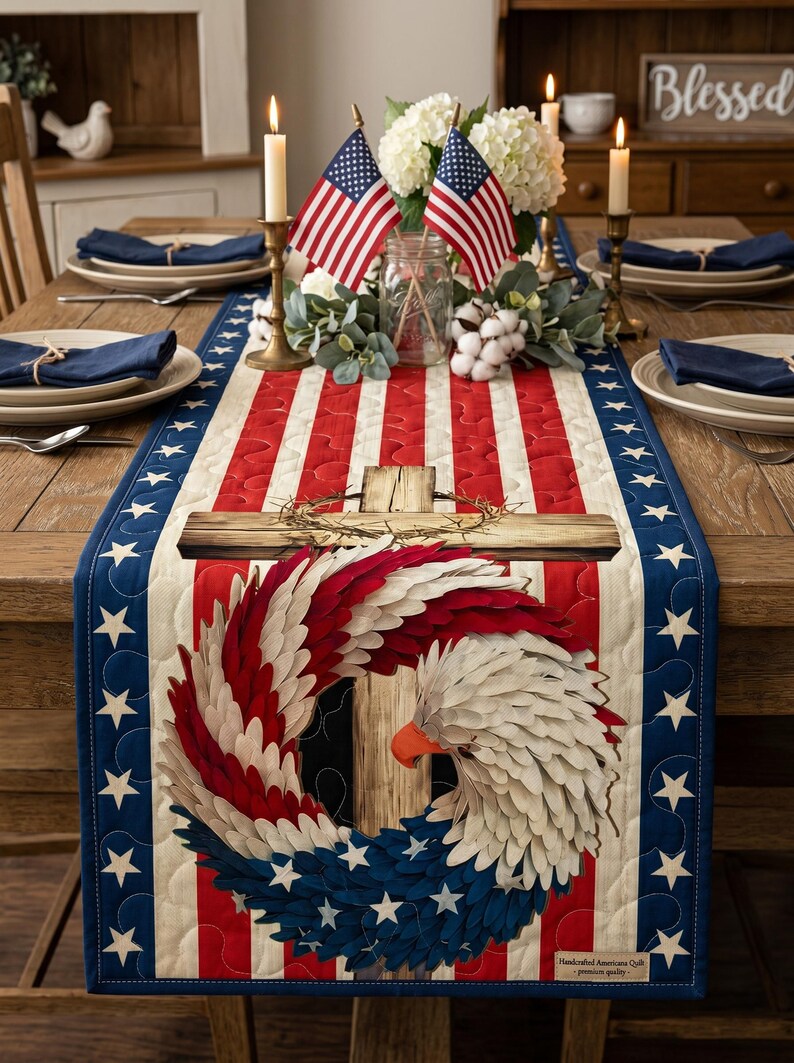 May include: A patriotic table runner with a red, white, and blue design. The center features a cross and an eagle with a wreath of feathers. The runner is bordered with blue fabric and white stars. The table is set with plates, napkins, and candles.