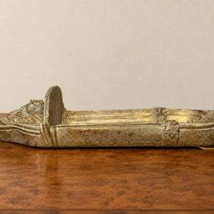 May include: A rectangular, boat-shaped decorative tray with a weathered, distressed gold and silver finish. The tray features a raised vertical divider at one end and ornate, sculpted relief details along the edges and the front section.