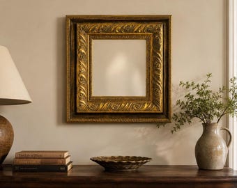 May include: A square wall mirror featuring a wide, ornate gold frame with a textured, repeating leaf-like pattern. The mirror has a reflective glass center and is mounted on a wall, positioned above a dark wooden dresser with books and a vase.