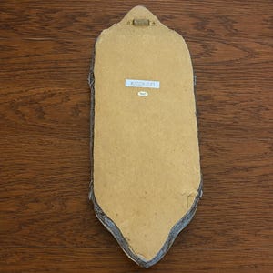May include: The back of an elongated, pointed-oval wall plaque featuring a tan fiberboard backing, a gold-toned metal hanging bracket at the top, and a white rectangular sticker printed with the text #2028-333 centered on the surface.