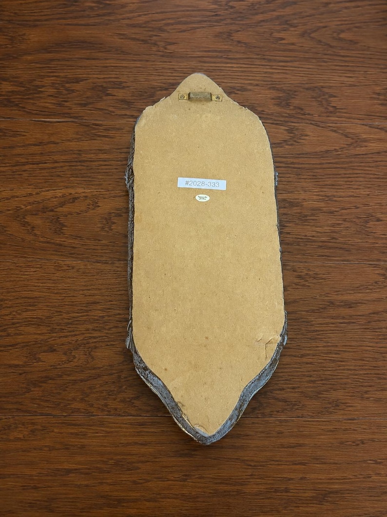 May include: The back of an elongated, pointed-oval wall plaque featuring a tan fiberboard backing, a gold-toned metal hanging bracket at the top, and a white rectangular sticker printed with the text #2028-333 centered on the surface.