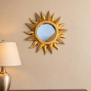 May include: A circular wall mirror featuring a gold-colored frame shaped like a sun with radiating pointed rays. The central glass is round and reflective, surrounded by a textured, metallic gold finish that mimics the appearance of sunbeams.