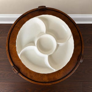 May include: A round, off-white ceramic serving platter featuring a central circular compartment surrounded by four distinct, curved sections. The outer rim of the platter is decorated with a subtle, embossed fan-like pattern along the edges.