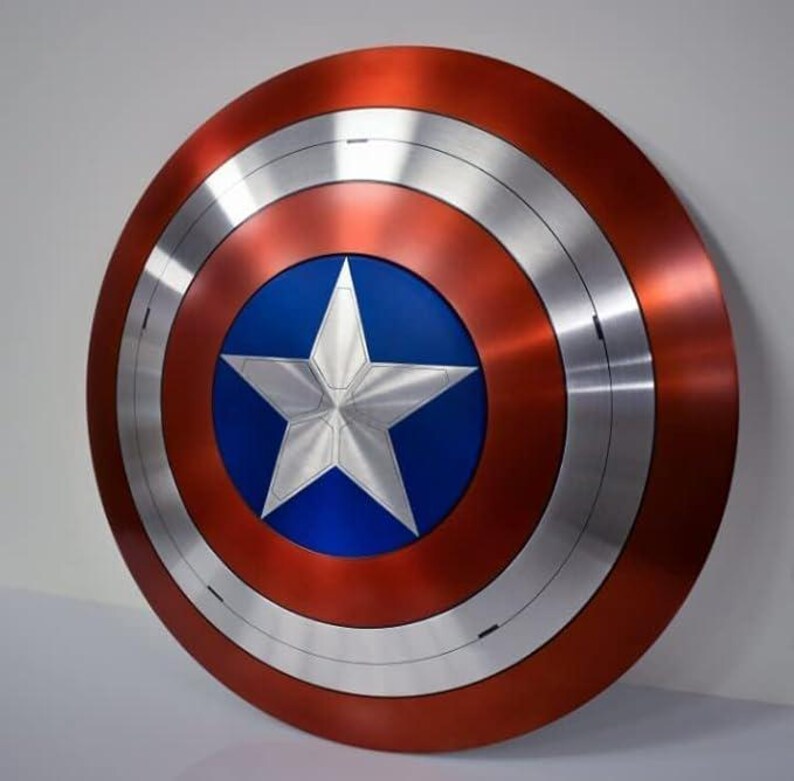 May include: A round shield with a red, silver, and blue color scheme. The shield features a large silver star in the center, set against a blue background. The outer ring is red, with silver bands separating the colors. A classic superhero accessory.