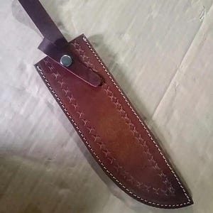 Peut inclure: Un &eacute;tui &agrave; couteau en cuir marron avec des coutures blanches et un motif d&eacute;coratif en forme d'&eacute;toile. L'&eacute;tui a une sangle avec une fermeture &agrave; bouton-pression en m&eacute;tal. L'&eacute;tui &agrave; couteau est con&ccedil;u pour prot&eacute;ger la lame.