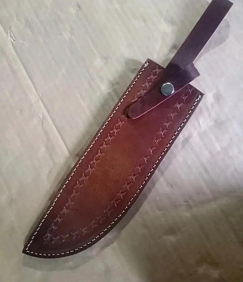 Peut inclure: Un &eacute;tui de couteau en cuir marron avec des coutures blanches et un motif en relief d&eacute;coratif. L'&eacute;tui est dot&eacute; d'une sangle avec une fermeture &agrave; bouton-pression. L'&eacute;tui est con&ccedil;u pour prot&eacute;ger la lame.