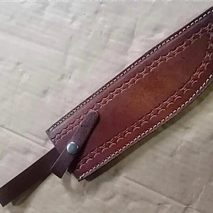 Peut inclure: Un &eacute;tui &agrave; couteau en cuir marron avec des coutures d&eacute;coratives et une fermeture &agrave; lani&egrave;re. L'&eacute;tui est con&ccedil;u pour contenir un couteau et pr&eacute;sente un motif d&eacute;taill&eacute; le long des bords et une sangle s&eacute;curis&eacute;e avec un bouton-pression en m&eacute;tal.