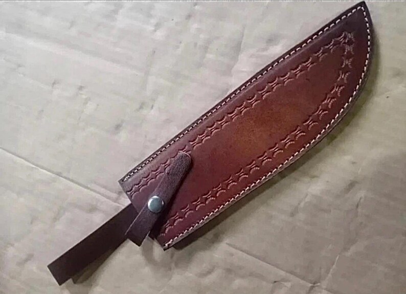 Peut inclure: Un &eacute;tui &agrave; couteau en cuir marron avec des coutures d&eacute;coratives et une fermeture &agrave; lani&egrave;re. L'&eacute;tui est con&ccedil;u pour contenir un couteau et pr&eacute;sente un motif d&eacute;taill&eacute; le long des bords et une sangle s&eacute;curis&eacute;e avec un bouton-pression en m&eacute;tal.