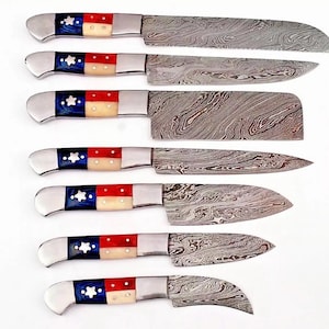Può includere: Un set di sette coltelli con lame in acciaio decorate. I manici presentano dettagli blu, bianchi e rossi. Il set comprende varie forme di lama, tra cui un coltello da macellaio e un coltello curvo.