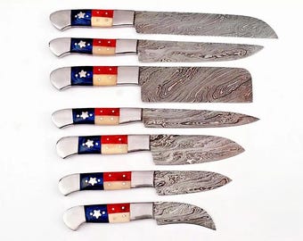 May include: A set of seven knives with patterned steel blades. The handles feature a design with blue, white, and red accents. The knives vary in size and shape, including a cleaver and a curved blade.